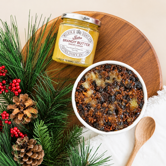 Jar of brandy butter with bowl of sticky pudding and holiday foliage.