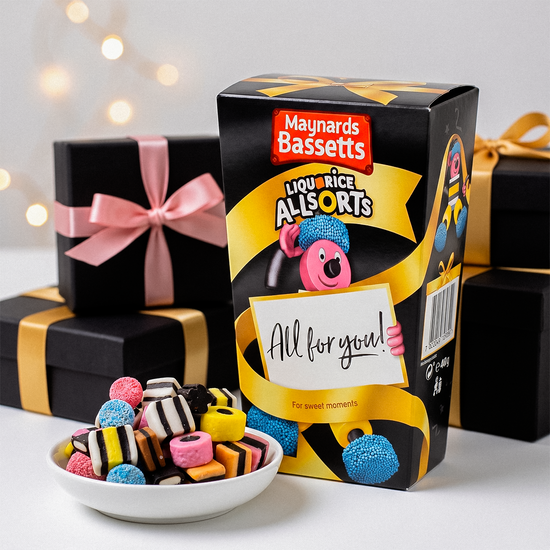Box of Maynards Bassetts Allsorts with a bowl of candies, black gift boxes, and festive lights.