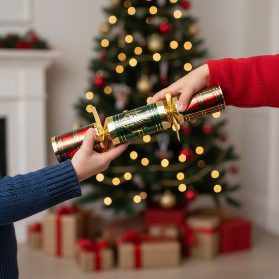 Two hands holding Christmas crackers in front of a decorated Christmas tree and fireplace.