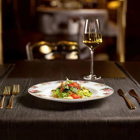 Dinner setting with a salad on a plate, wine glass, and cutlery on a table.