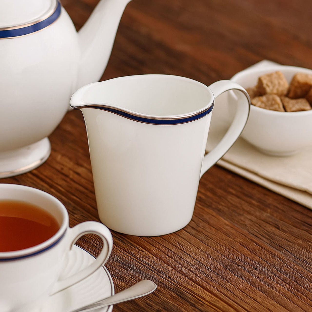 Tea set with teapot, cup, and creamer on a wooden table.