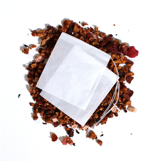 White tea bag surrounded by dried herbs on a white background