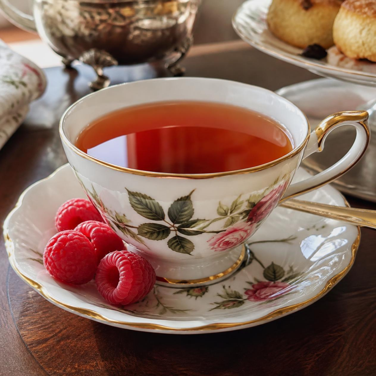 Hot Raspberry Black Tea in a Teacup with raspberries on the side and in the upper corner scones.