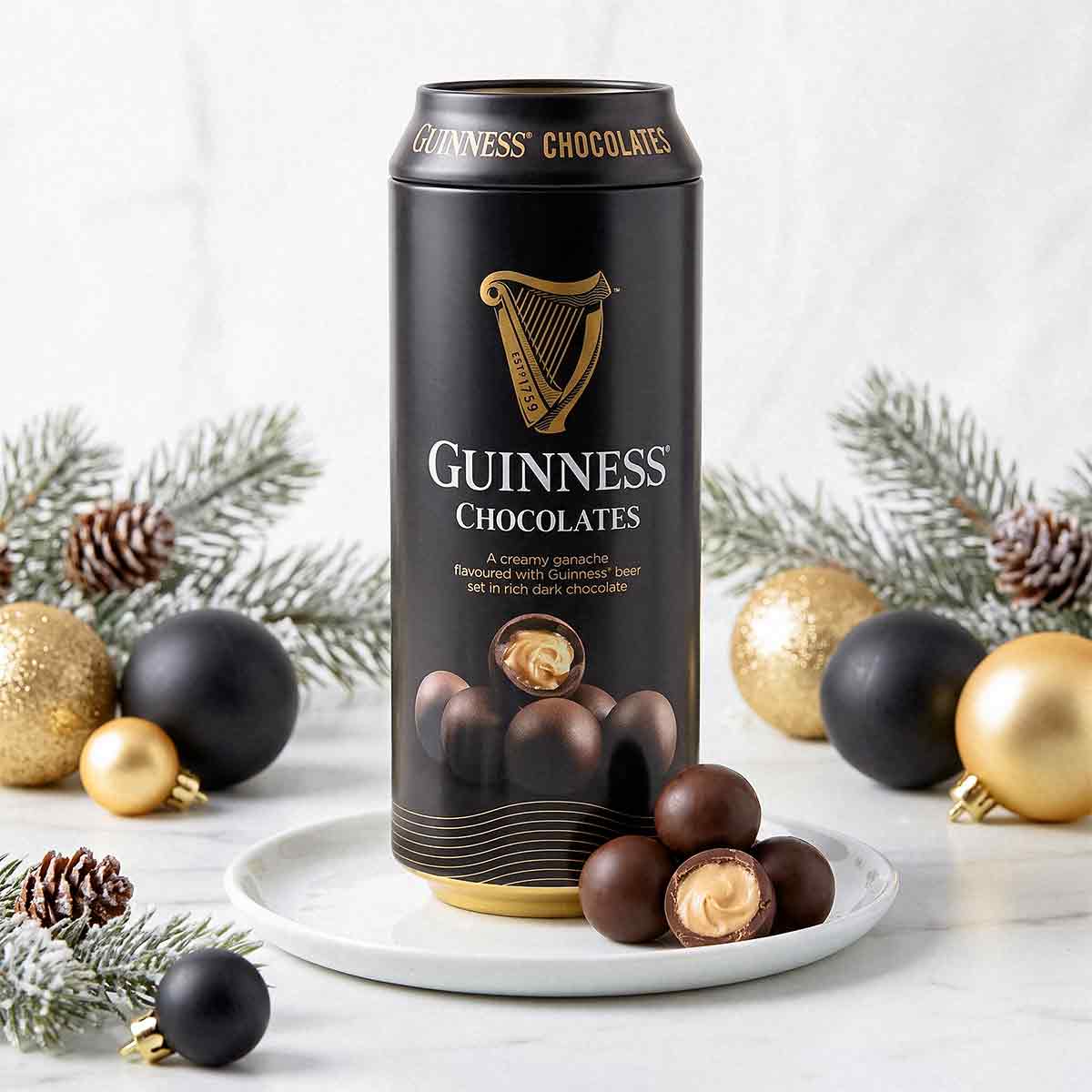 Guinness Chocolates tin on a white plate with chocolates, surrounded by festive greenery, pine cones, and gold and black baubles