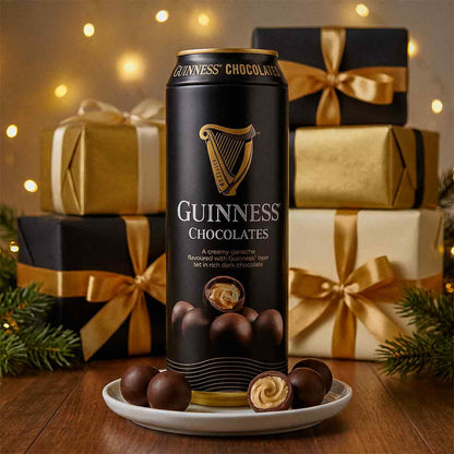 Guinness Chocolates tin on a white plate with chocolates, with wrapped gifts, fairy lights, and pine branches in the background