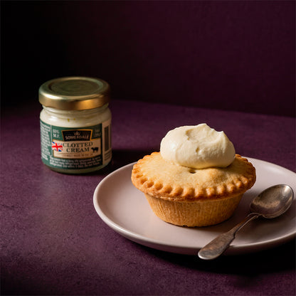 Mince pie topped with clotted cream on a plate beside a jar of cream.