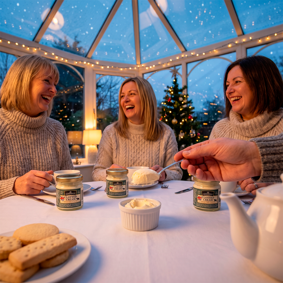 Women at a table in a conservatory with fairy lights, jars of clotted cream and a hand spooning cream.