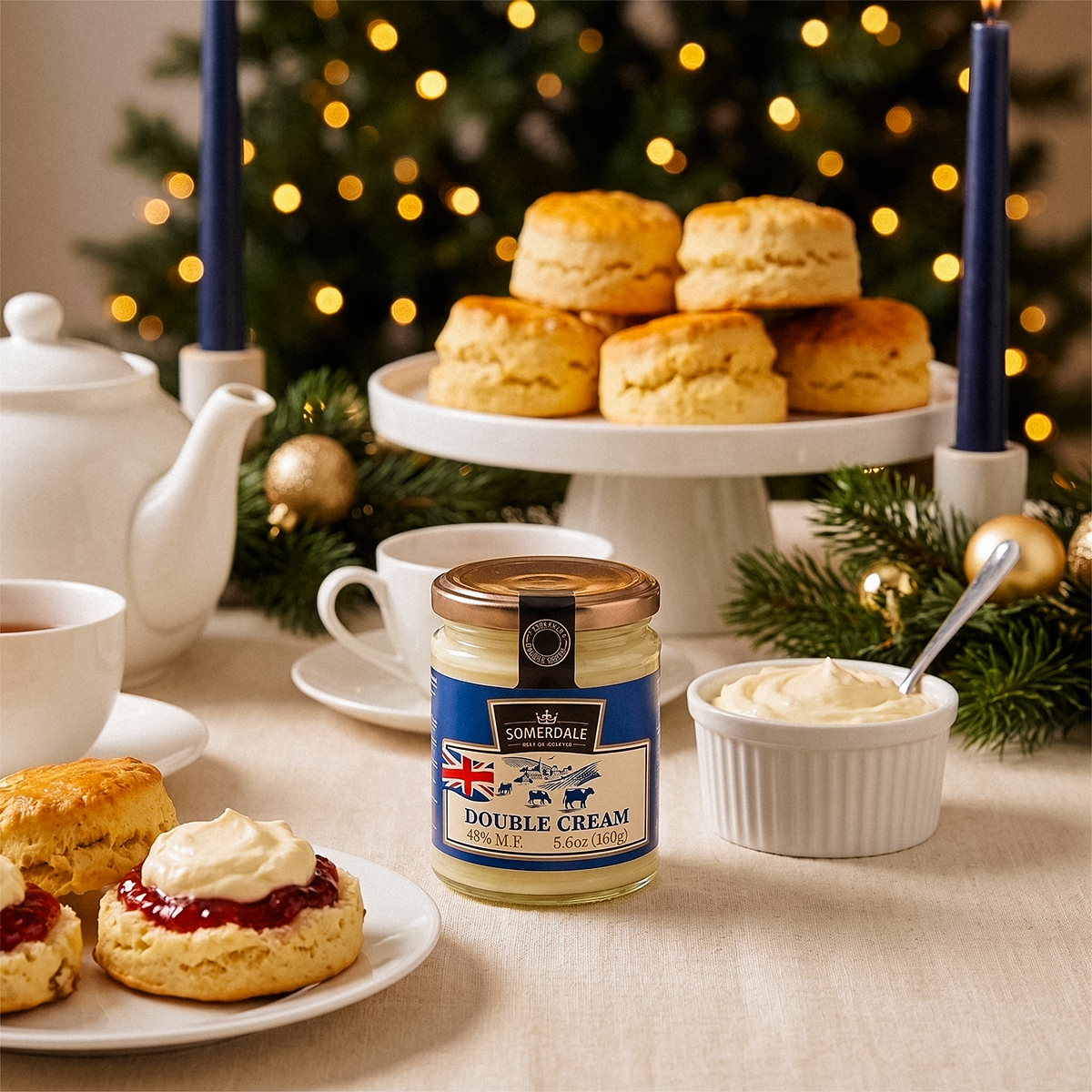 Jar and bowl of cream with scones on a cake stand, teapot, and Christmas tree behind