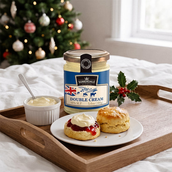 Jar and bowl of cream with scones on a wooden tray, Christmas tree and snowy window behind