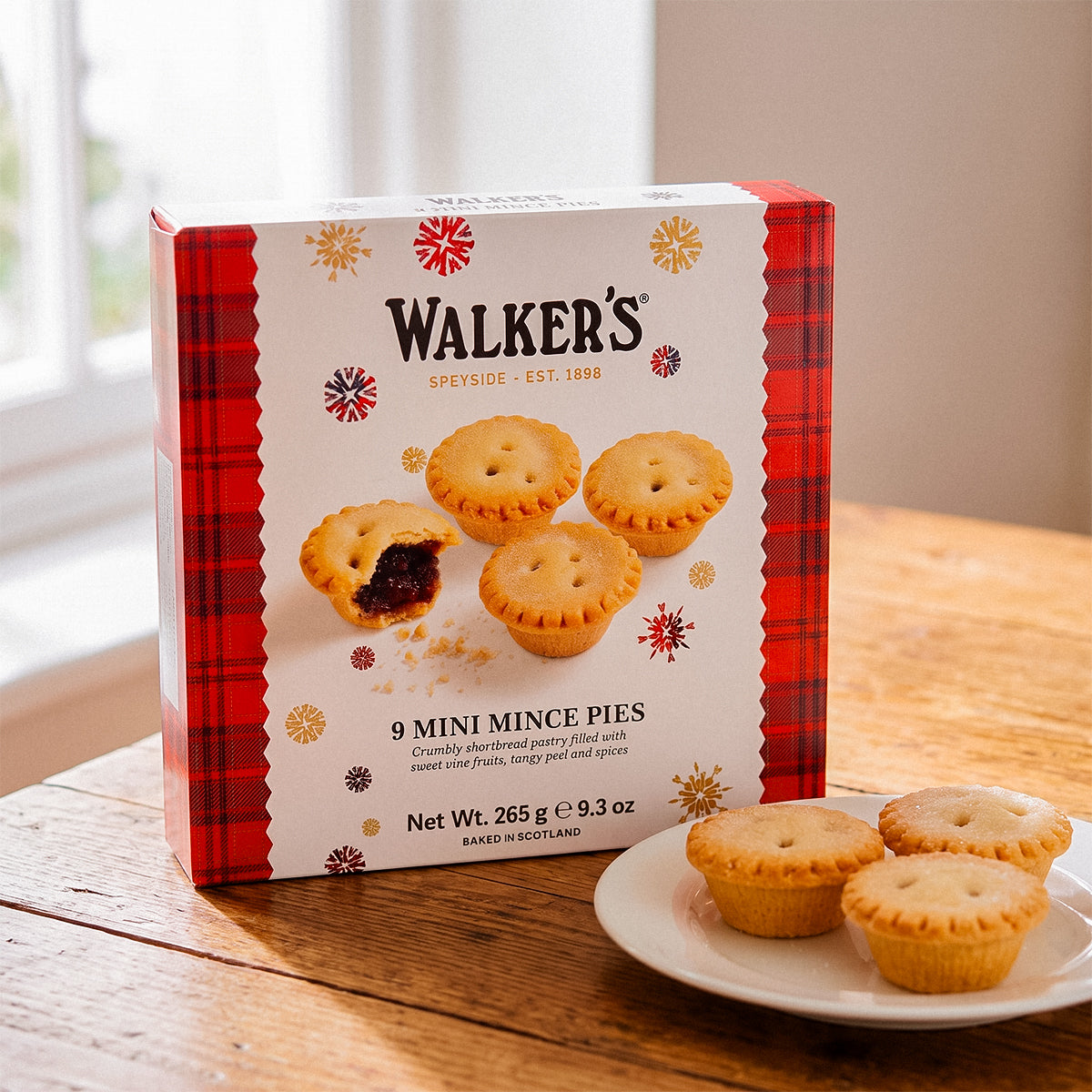 Box of Walker’s 9 Mini Mince Pies on a wooden table with a plate of three mince pies.