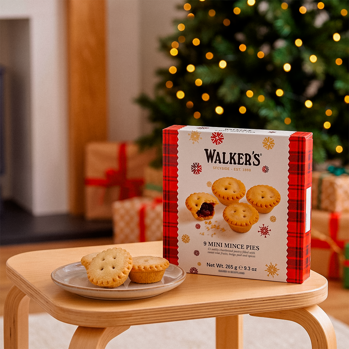 Walker’s 9 Mini Mince Pies box on a small stool with a plate of two pies, Christmas tree in the background.