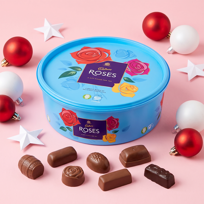 Blue Roses chocolate tub with scattered chocolates, baubles, and stars on a pink background