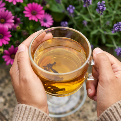 A person holding a clear glass of herbal tea.