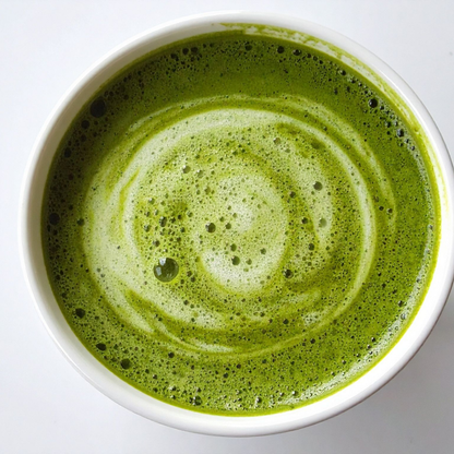 A top-down view of a white ceramic cup filled with a frothy green matcha latte, showing a swirled pattern of foam on the surface.