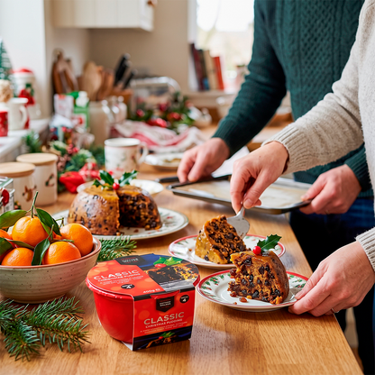 People at a table cutting a Christmas pudding, with a red tub, oranges, and festive decorations