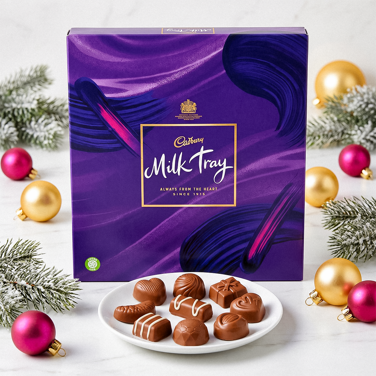 Purple Milk Tray box with a plate of chocolates, baubles, and pine sprigs on a white surface