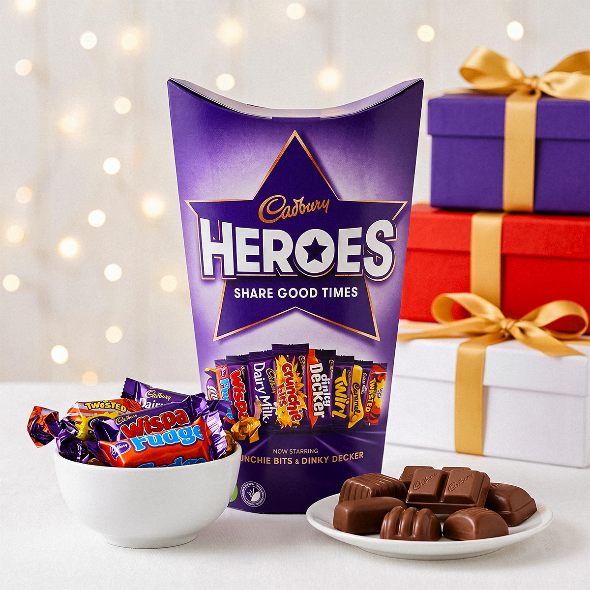 Cadbury Heroes box with a bowl of chocolates, a plate of chocolates, and wrapped gifts behind