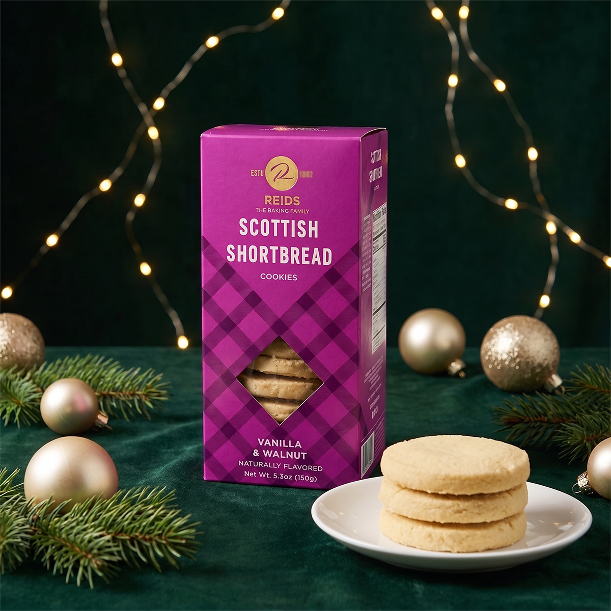 Purple Scottish Shortbread box on a dark green surface with a plate of shortbread, pine sprigs, gold baubles, and fairy lights