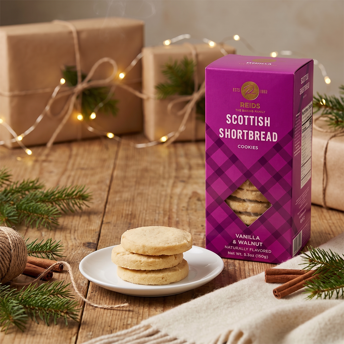 Scottish Shortbread box on a wooden table with a plate of shortbread, a candle, and a wrapped gift