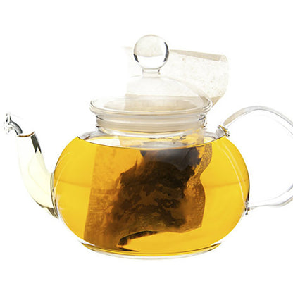 Clear glass teapot with a lid filled with yellow hot tea leaves and a tea bag.