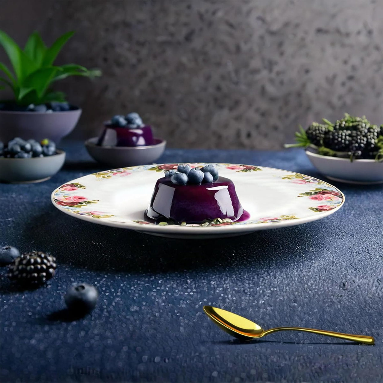 Decorative plate with a dessert and blueberries on a dark surface, with a gold spoon in the foreground.