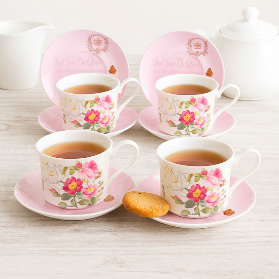 Set of four floral teacups and saucers with pink borders on a light wooden surface.