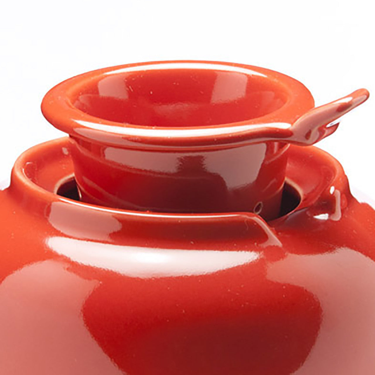Close up of the top of a red ceramic teapot with an infuser on a white background