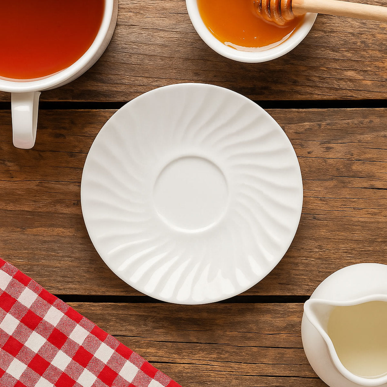 White porcelain saucer on a wooden table with a cup of tea, honey, and a checkered cloth.