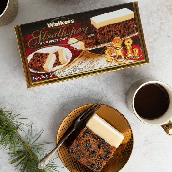 Box of walkers fruit cake with a cup of hot tea and a plate with a slice of cake on it