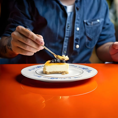 Person eating a slice of cheesecake with a fork on an orange table