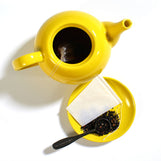 A pack of white drawstring tea filters displayed alongside a clear teapot with tea bags inside, indicating usage.